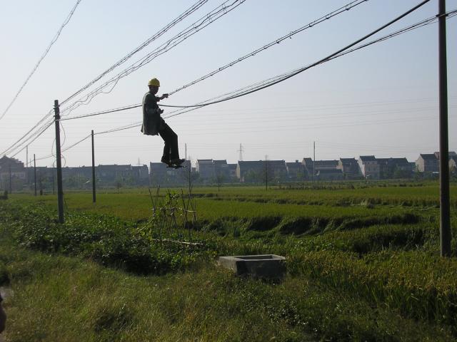 Oct 2007 - Hanging loose, a Chinese electrical worker repairs the easy way, sliding along the line without a ladder.