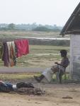 A farmer rests in the shade of his mud hut.