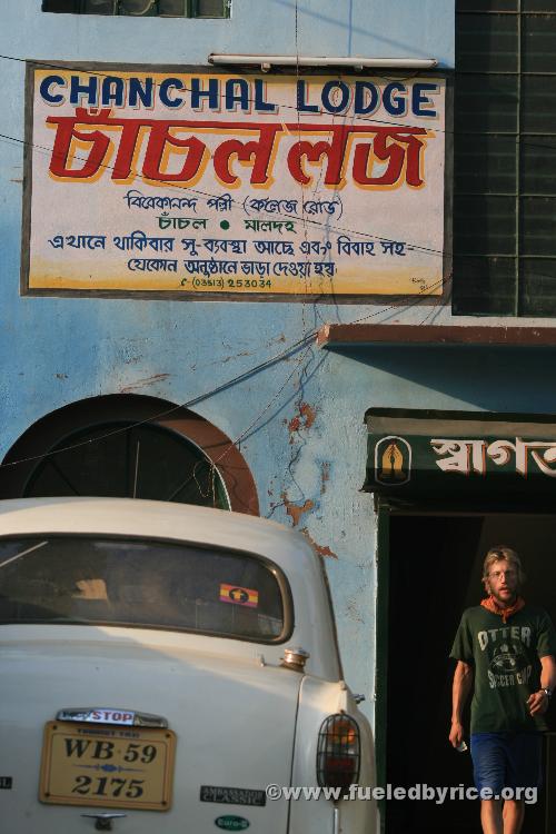 India, West Bengal, Chanchal town - Drew walking out of our cheap guesthouse with a typical Ambassador Classic car parked in fro